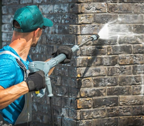 man pressure washing a wall